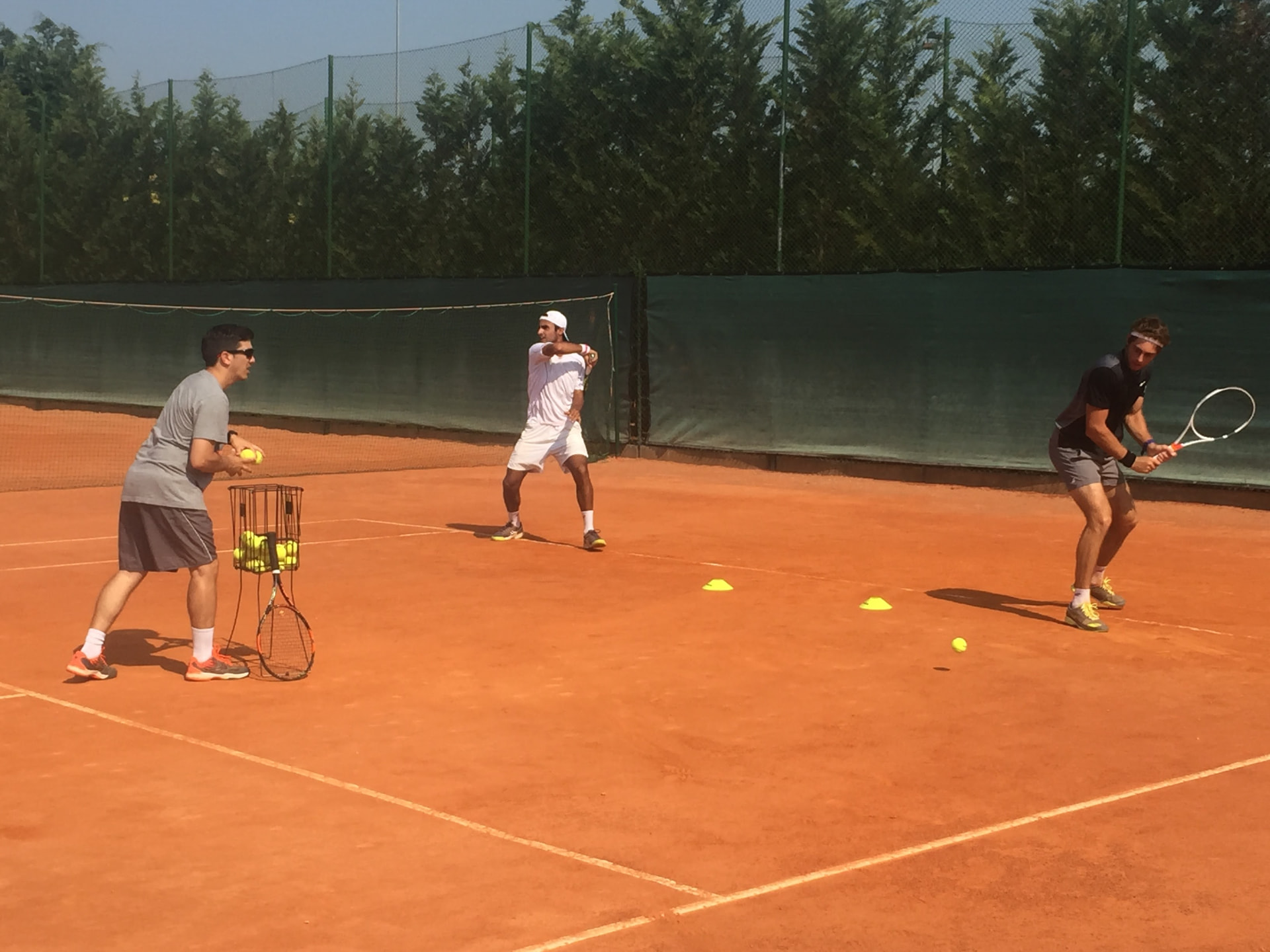 Luciano Perticarolli entrenando a dos jugadores profesionales en una pista de tierra batida